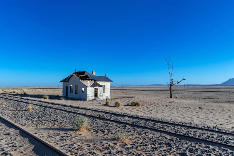 Alte Bahngleise führen durch die Wüste auf ein einzelnes Haus zu